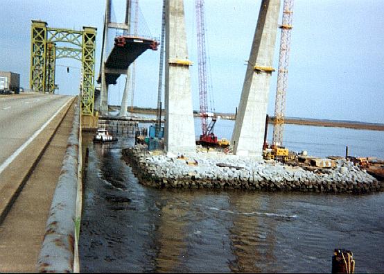 Wide view of south island with cranes and construction equipment dotting it, old bridge is dwarfed by comparison